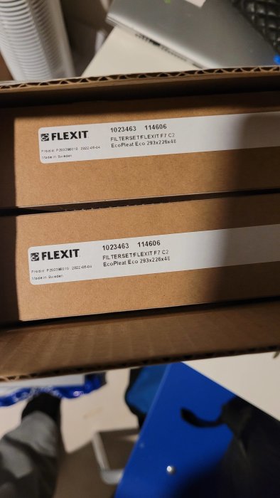 Två kartonger med etiketter, text "FLEXIT", tillverkade i Sverige, på ett oordnat kontor.