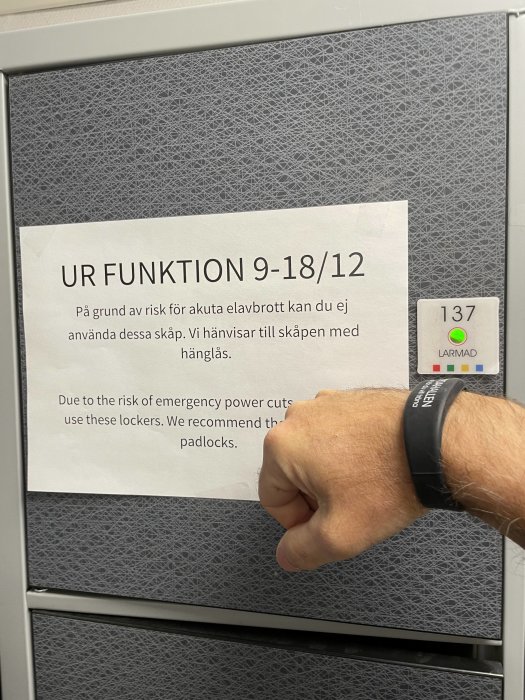En hand pekar på ett meddelande på skåp, varnar för elavbrott, rekommenderar användning av hänglås.