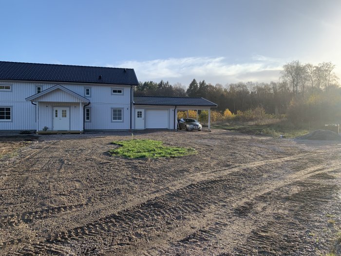 Stort vitt hus, garage, uppgraderad mark, bil under tak, träd med höstfärger.