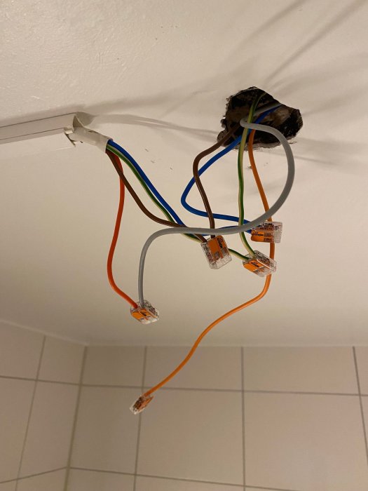 Elektriska kablar hänger från hål i tak, kopplade med skarvklämmor, otillfredsställande elinstallation, vit bakgrund.