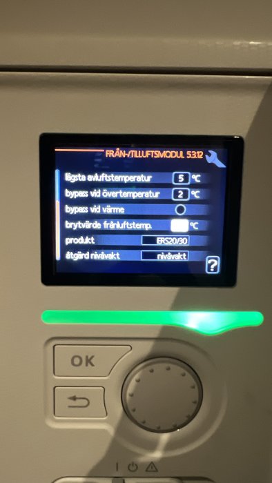 Digital kontrollpanel för ventilationssystem som visar inställningar och temperaturinformation på svenska. Knappar och grön indikatorlampa syns nedanför.