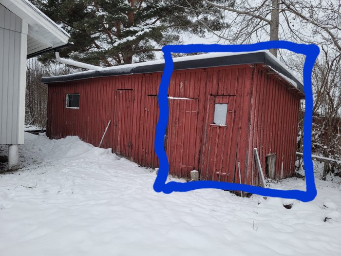 Röd snötäckt lada med vit dörr, trädetaljer och blå markeringslinje på bilden.