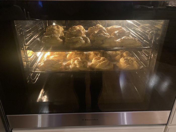 En upplyst ugn fylld med bullar på flera bakplåtar, troligen under bakning.