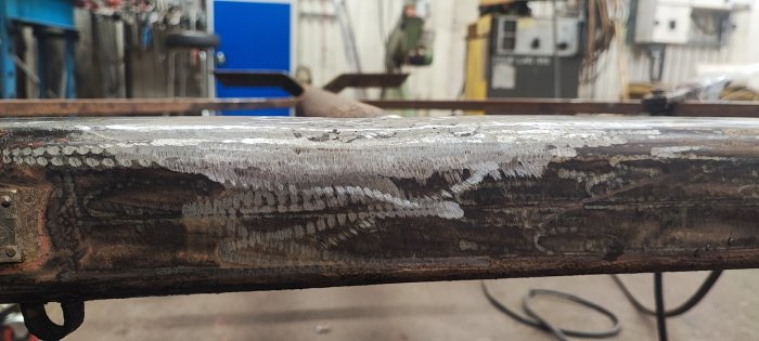 Metallstång med svetsfogar, grov yta, industriell miljö, verkstad, bearbetning av material, svetsningsteknik i förgrunden.