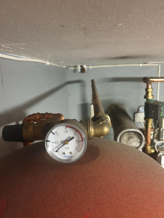 Manometer på rörsystem, visar tryck, installerad på tank, industriell miljö, rörledningar och ventiler i bakgrunden.