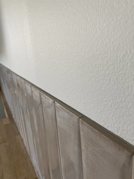 Vit texturerad vägg ovanför beige kakel, trägolv, interiör, hörnperspektiv, inomhus, minimalistisk design.