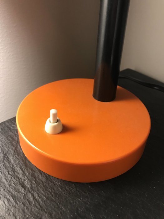 Orange, rund bas, svart stång, minimalistisk design, lampa eller högtalarstativ, enkel, modern, detaljbild, inomhus.