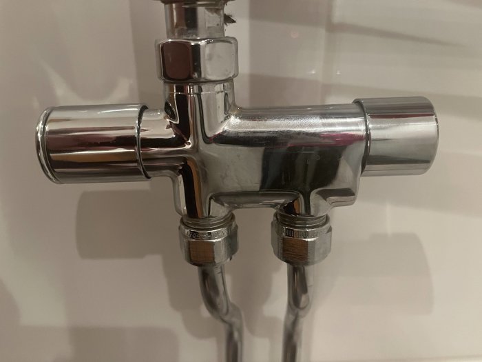 Kromad termostatisk blandventil eller duschblandare, mot en vägg, med en reflekterande yta.