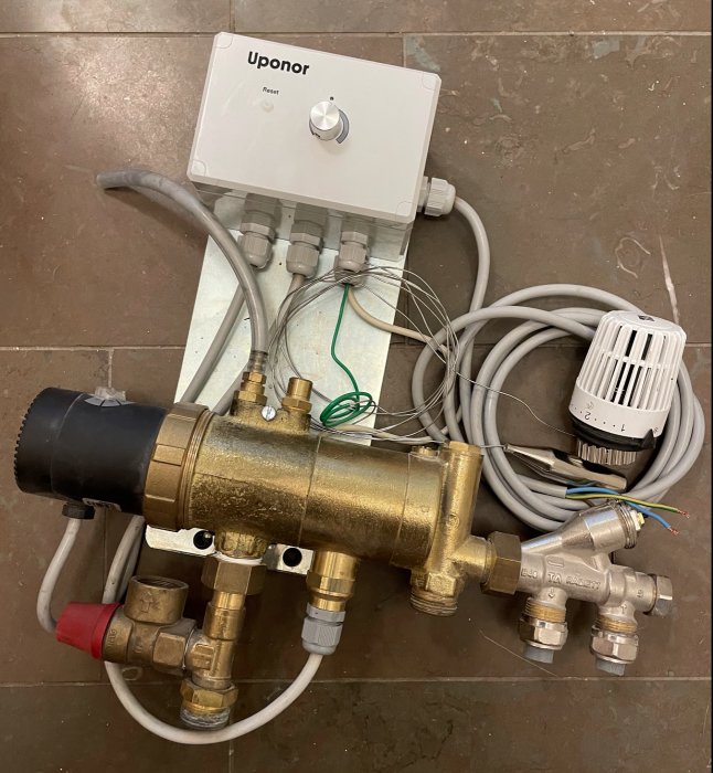 Uponor värmesystemkomponenter på golv: styrbox, mässingsfördelare, kablar, termostatisk ventil.