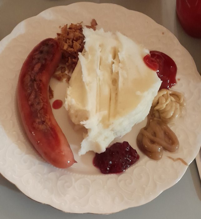 En tallrik med korv, potatismos, stekt lök, lingonsylt och ketchup.