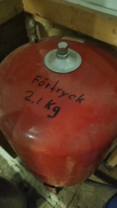 Röd trycktank märkt "Förtryck 2.1 kg", skruv på topp, placerad på smutsigt underlag.