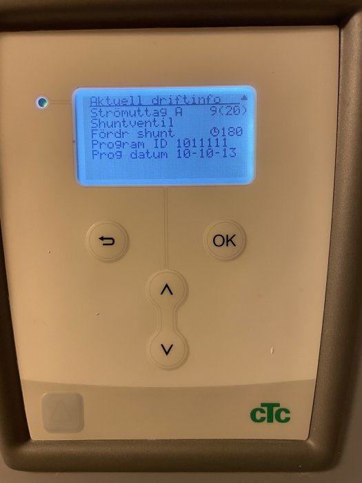 Fjärrvärmecentralens display visar driftinformation, temperatur, flöde och programdatum. Knappar för navigering syns nedanför.