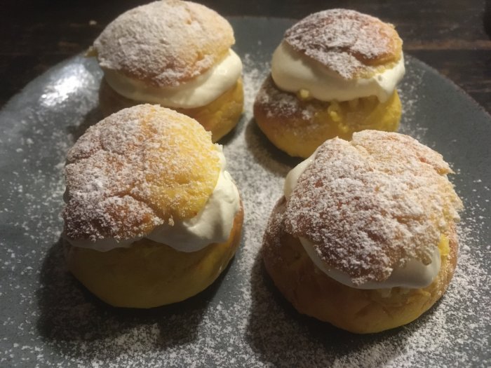 Fyra semlor med florsocker på mörk tallrik. Traditional Swedish cream-filled pastry.