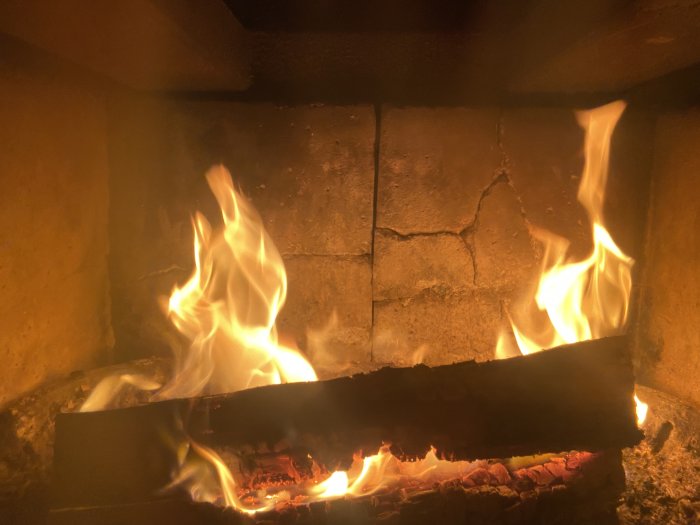 En öppen eld i en spis, med flammande ved och glödande kol. Värme och mysighet i en bild.