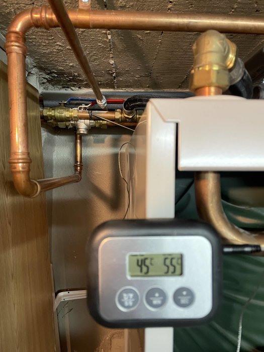 Varmvattenberedare med kopparledningar, display visar temperaturer 45°C och 55°C, teknisk utrustning i hemmet.