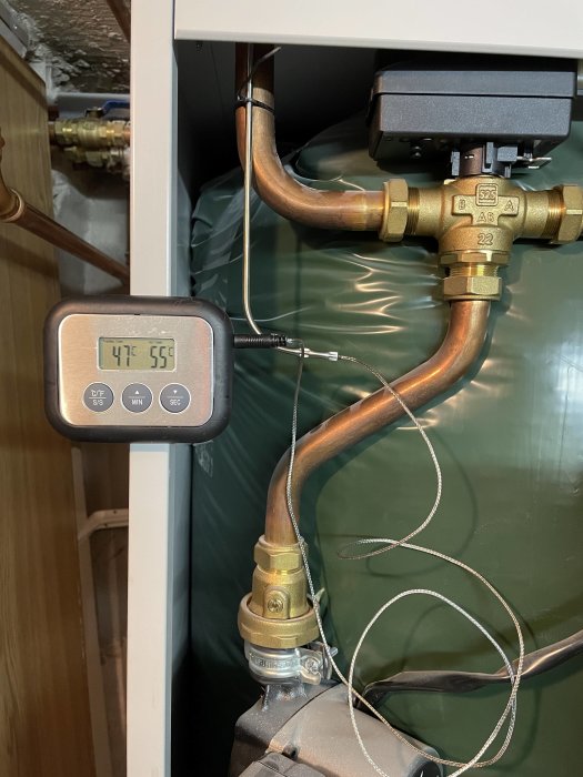 Värmesystem med rör, termometerskärm som visar tid och temperatur, och ventiler.