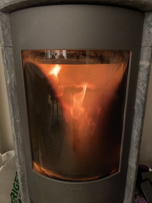 Eld i en modern braskamin, ljuset reflekterar i genomskinligt material, med en sotig glasyta.