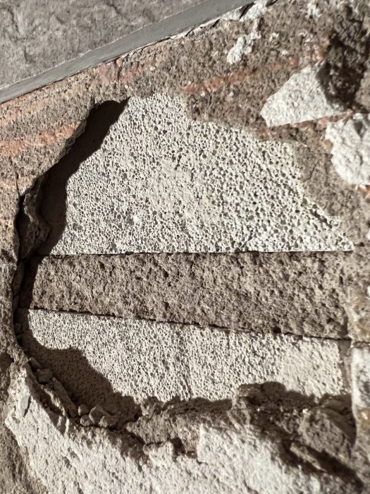 En närbild av en skadad eller sliten betongvägg med tydliga sprickor och avbruten yta.
