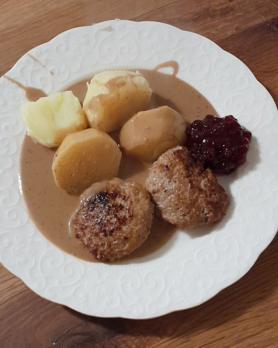 Svensk köttbullar, potatis, brunsås och lingonsylt på ett vitt mönstrat tallrik.