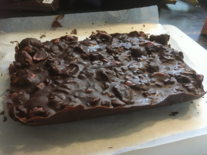 Stor chokladkaka med nötter, hemlagad, kylt på bakplåtspapper, ojämn yta, mörkt utseende.