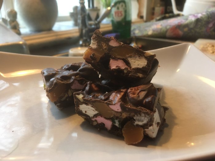 Chokladgodis med marshmallows och nötter på vit tallrik, oklart bakgrundsföremål, inomhus och dagsljus.