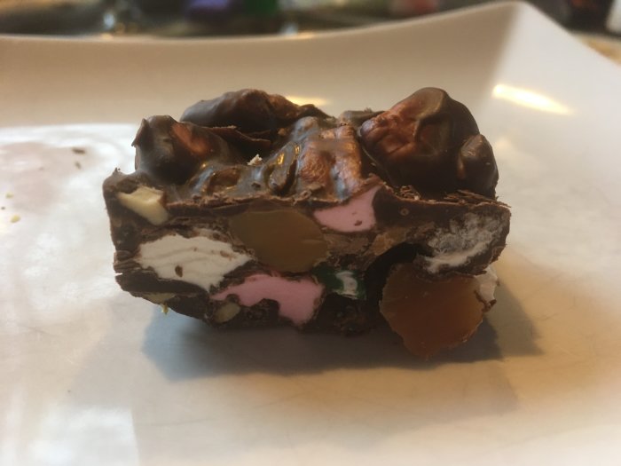Ett stycke chokladgodis med nötter och olika fyllningar på en vit tallrik.