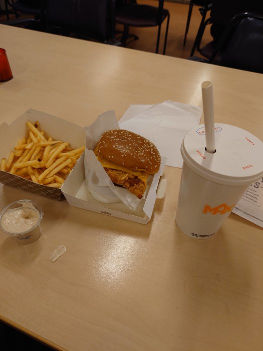 Snabbmatsmåltid med hamburgare, pommes frites, dryck och sås på ett bord.