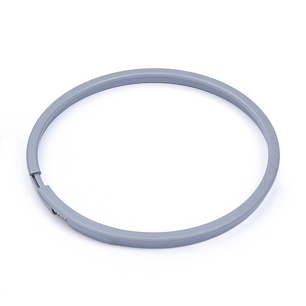 Grå rund plastseal med öppning, troligen maskindel eller tätning, ensfärgad bakgrund.