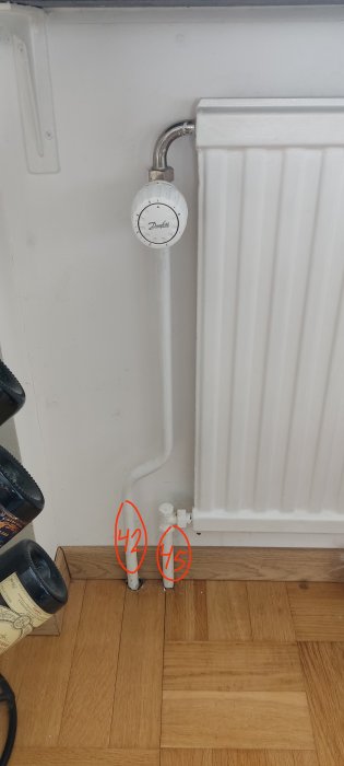 Vit element med termostat och rör på trägolv, vägg bakgrund. Röda siffror ritade på bilden.