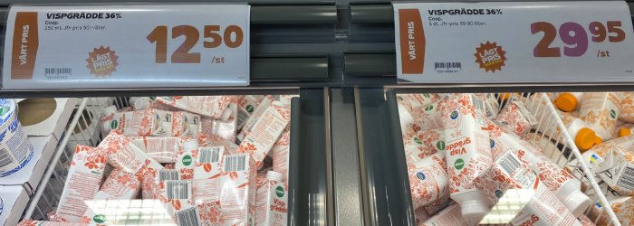 Butikshylla med vispgrädde, prisinformation. Två olika priser visar prisskillnad. Coop-märke synligt.