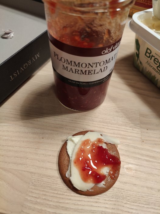 Knäckebröd med ost och plommon- och tomatmarmelad. En bok och smörburk syns också.