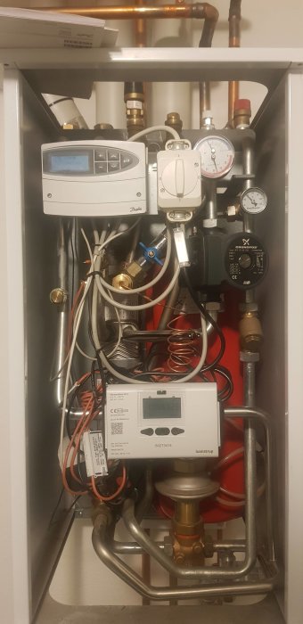 Värmepanna med rör, mätare och elektronisk kontrollpanel inuti ett skåp. Installationsdetaljer och teknisk utrustning synliga.