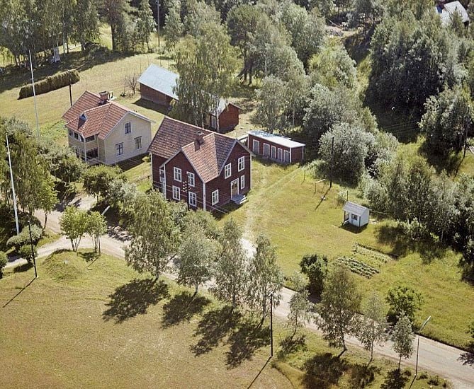 Flygbild på lantligt område med hus, träd, en väg och gröna ytor.