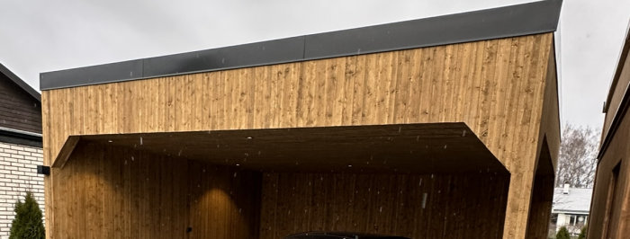 Modernt träbeklätt hus med skarp arkitektur, grå himmel, detaljbild, möjligt carport eller entré.