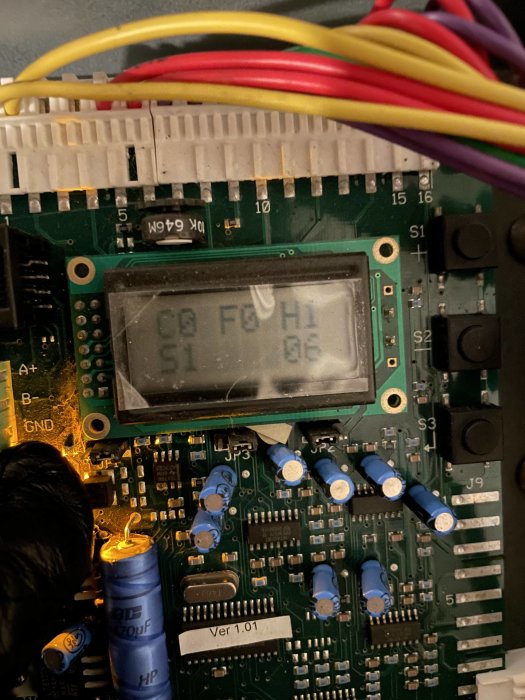 Elektronikkrets med display, kondensatorer och färgade kablar. Indikerar en teknisk eller elektrisk enhet. Ver 1.01.