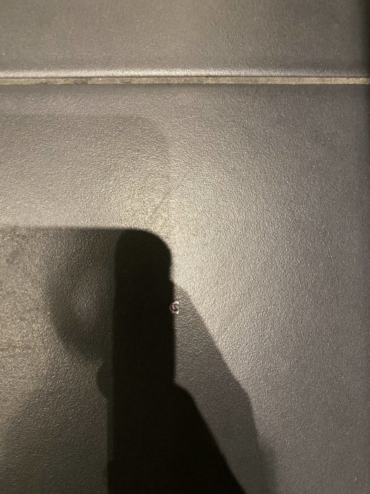 Skugga av en person mot en texturerad grå vägg, markerad av ljus och mörker.