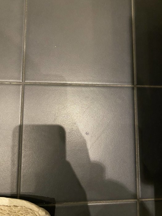 Grå klinkergolv med skugga av en person och del av möbel eller objekt.