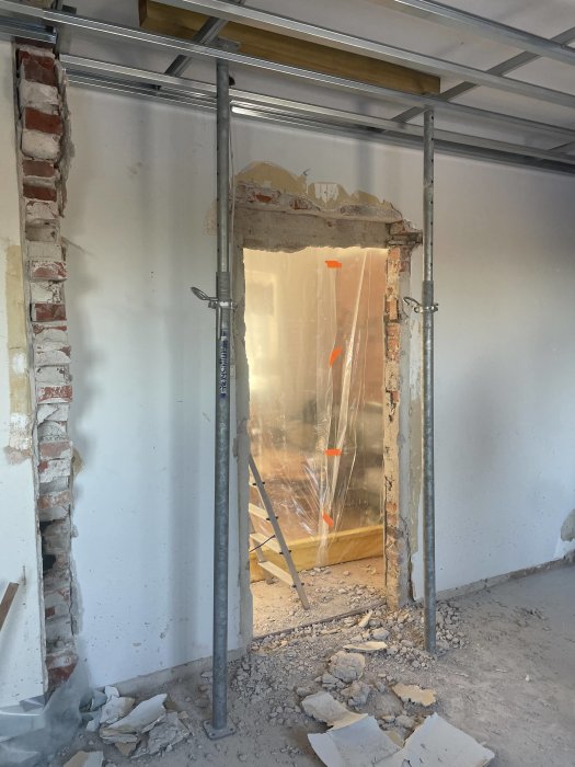 Renovering pågår, vägg nedbruten, stödställningar, byggplast, rörbitar, byggdamm och esbest ser ut att skyddas.