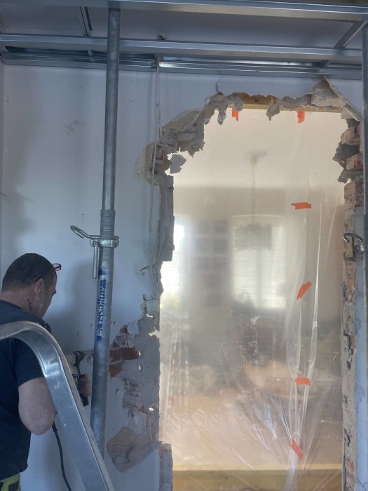 Person arbetar vid delvis rivet vägguttag, byggarbetsplats med skyddsplast och byggnadsställning inomhus.