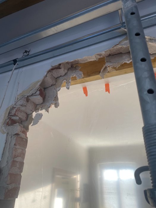 Skadad vägg och puts med synligt trä och tegel, skenbart i en byggnation eller reparation, med ställningsrör.