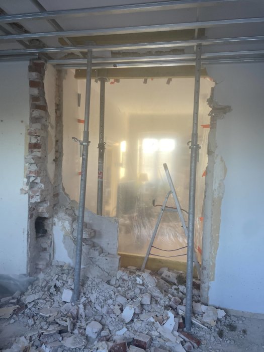 Byggplats inomhus med rivna väggar, rasmassor, ställning och stege, dammigt och under konstruktion eller renovering.