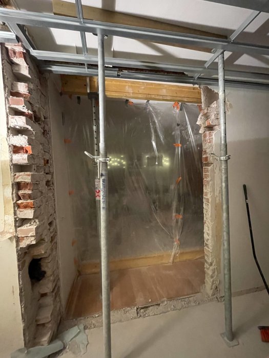Renovering pågår: Inslag av stöttor, naken tegelvägg, plastskydd, och byggställning av metall mot taket.