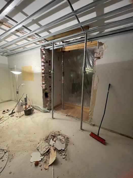 Renoveringsarbete pågår med exponerade gipsskivor, öppet tak och byggmaterial på betonggolvet.