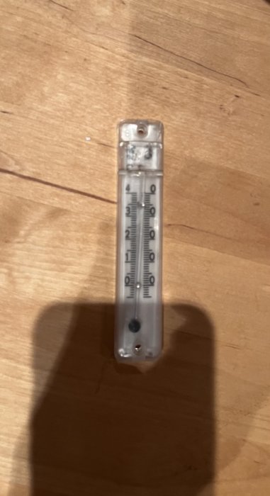 Transparent termometer på trät underlag, grader Celsius, lodrät position, skugga till höger, oskarp närbild.