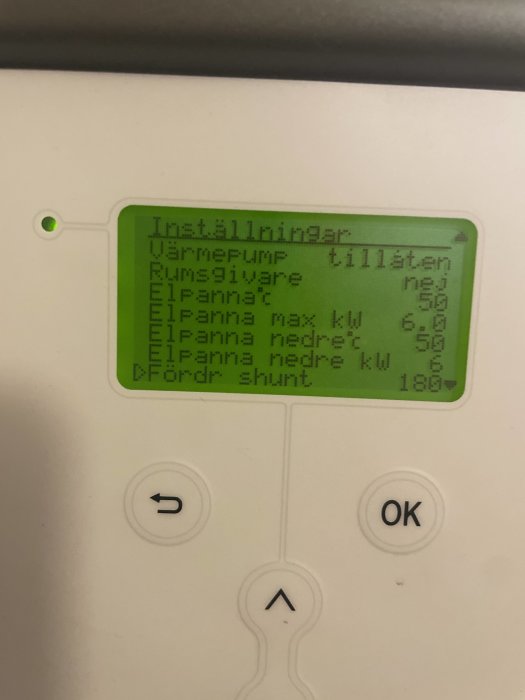 Grön monokrom display på värmepumpsstyrning visar temperaturinställningar och knappar för navigering.