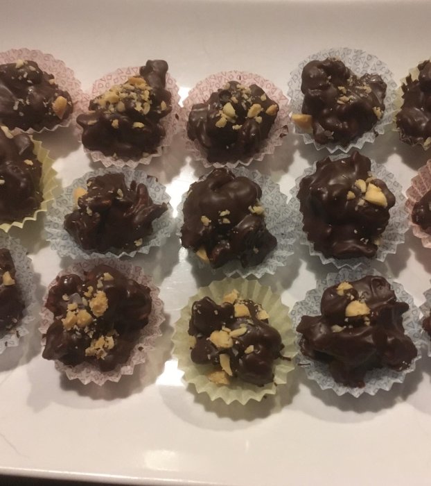 Chokladdragerade konfektyrer med hackade nötter, serverade i pappersformar på ett fat.