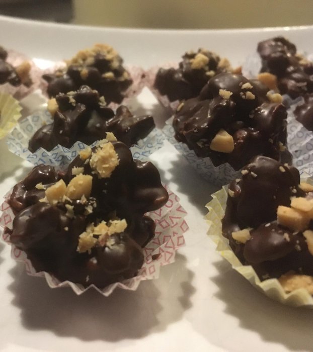 Chokladpraliner i små bakformar, toppade med hackade nötter, serverade på ett vitt fat.