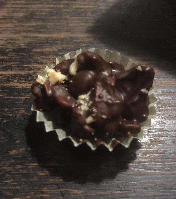 Mörk chokladgodis med nötter i folieform på träyta. Fokus på mitten, oskarp i för- och bakgrund.