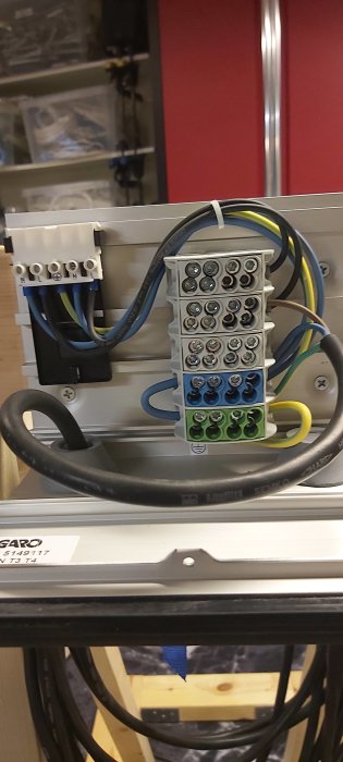 Elektrisk kopplingsdosa med terminalblock och kablar, monterad på metallram, i teknisk miljö.