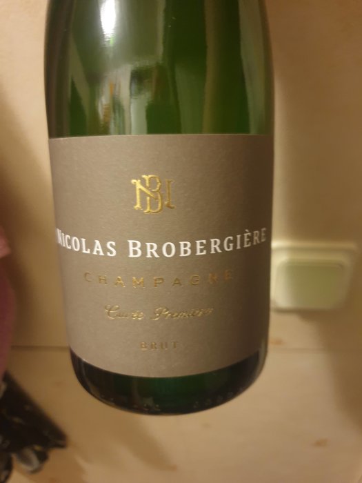 Champagneflaska, Nicolas Brobergiere, grön, etikett, "Cuvée Première Brut", otydlig, guldbokstäver, närbild, inomhus.